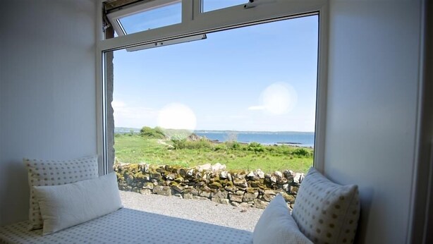 A room with a bed facing a stone wall and a view of a grassy landscape.
