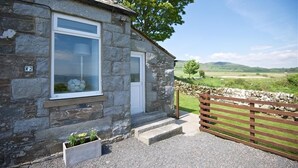 A stone house with a white door and windows, a gravel driveway, and a wooden fence.