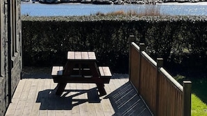 A wooden deck with a picnic table overlooking a lake and mountains. - The Lodge -  a lodge that sleeps 6 guests  in 3 bedrooms (Lochgilphead)