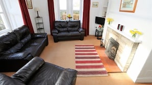 A living room with a fireplace, a sofa, a TV, and a window with curtains. - The Lodge -  a lodge that sleeps 6 guests  in 3 bedrooms (Lochgilphead)