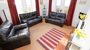 A living room with two black leather sofas, a striped rug, and a small table with yellow flowers. - The Lodge -  a lodge that sleeps 6 guests  in 3 bedrooms (Lochgilphead)