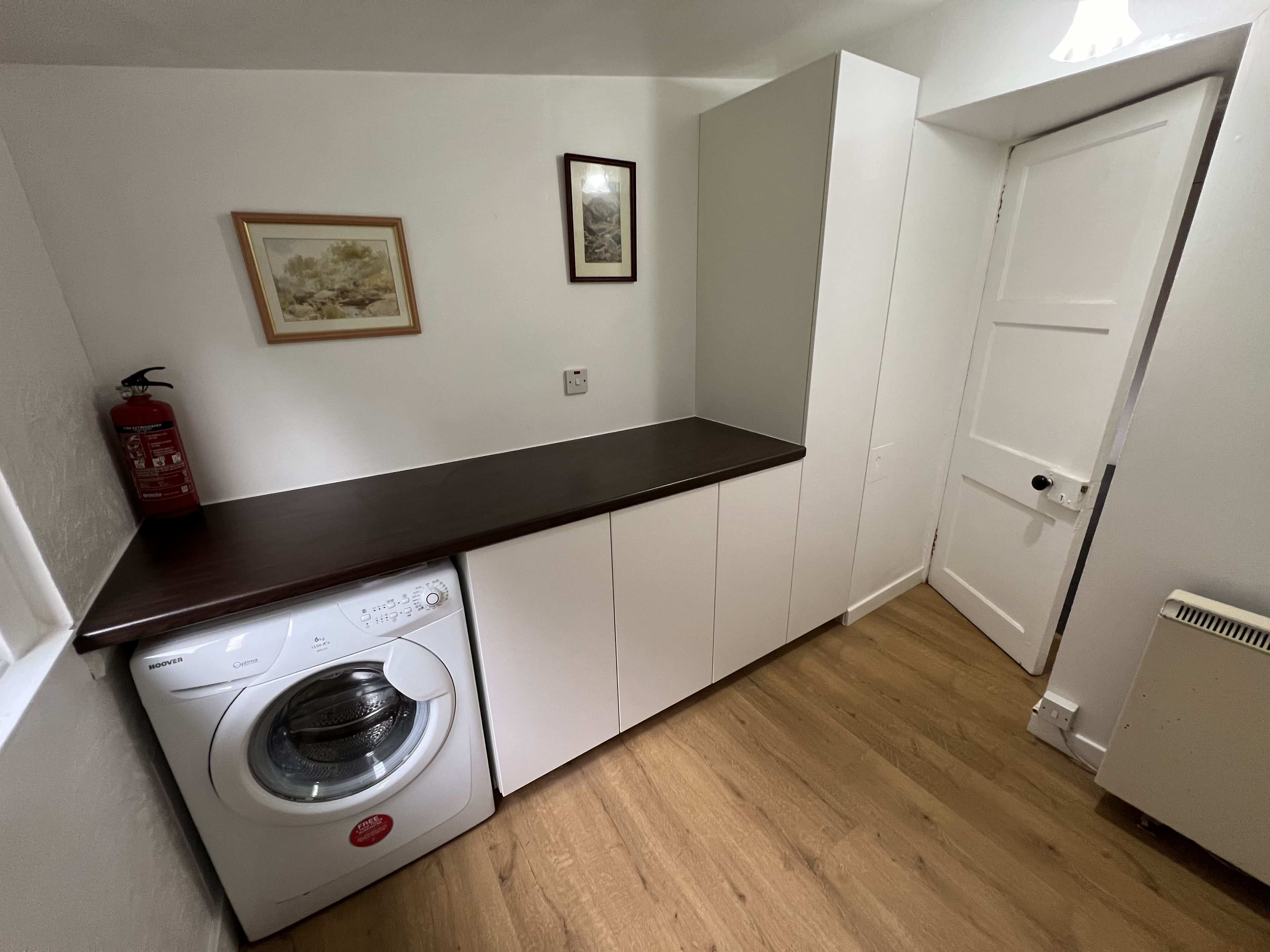 A compact kitchen with a washing machine, a fire extinguisher, and a door.