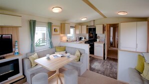 Interior compacte d'una caravana amb zona de menjador, petita cuina i televisor.
