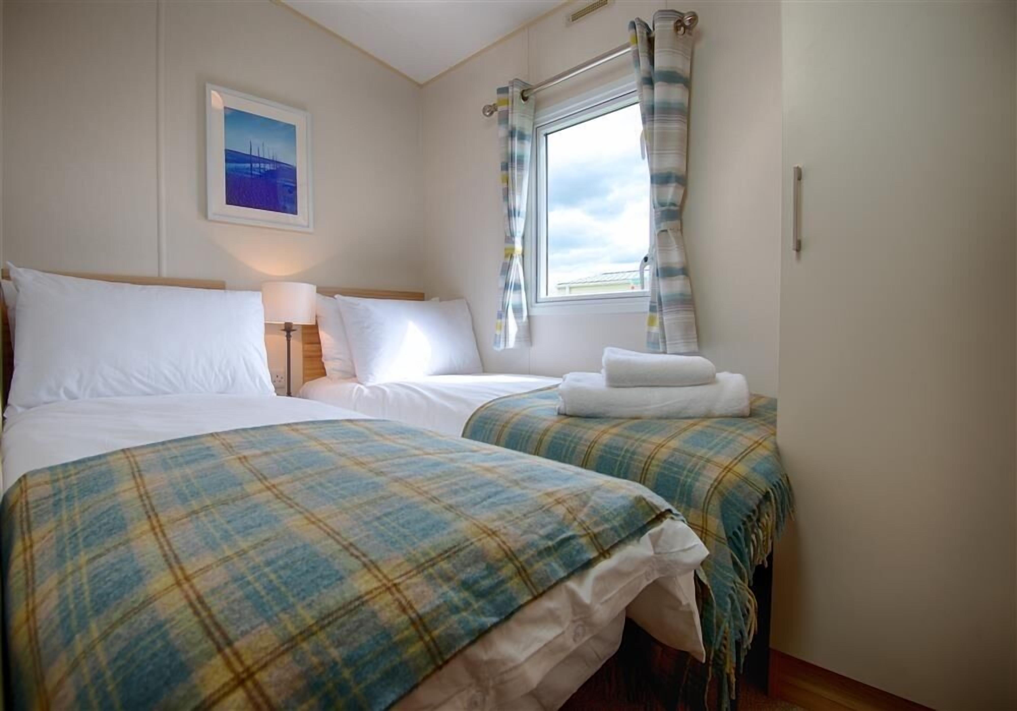 A hotel room with two beds, a window with curtains, a bedside lamp, and a framed picture on the wall.
