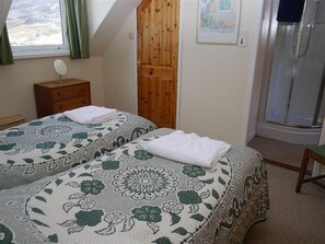 A bedroom with two beds, a wooden door, a small bedside table, a framed picture on the wall, and a shower area. - Sangobeag -  a cottage that sleeps 6 guests  in 3 bedrooms (Durness)