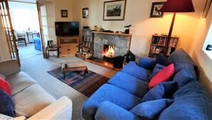 A living room with a fireplace, a television, and a bookshelf. - Sangobeag -  a cottage that sleeps 6 guests  in 3 bedrooms (Durness)
