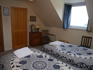 A bedroom with two beds, a dresser, a chair, a window with curtains, and a door. - Sangobeag - a cottage that sleeps 6 guests in 3 bedrooms (Durness)