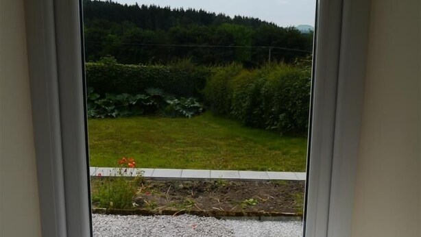 Ein Fenster mit Blick auf eine grüne Landschaft, eine schwarze Schale und ein Glas mit einem Getränk auf einem Fensterbrett.