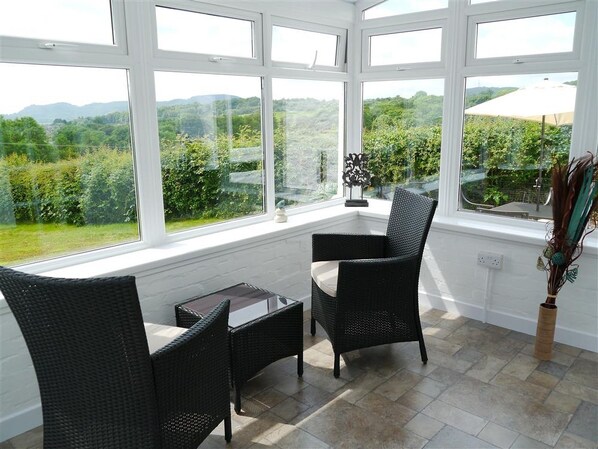 A conservatory with a view of a green landscape, furnished with wicker chairs and a glass table. - Swallow Cottage - a cottage that sleeps 6 guests in 3 bedrooms (Dalbeattie)