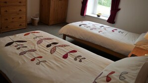 Ein Schlafzimmer mit zwei Betten, einer Holzkommode, einem Kleiderschrank und einem Fenster mit Vorhängen.