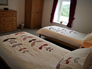 A bedroom with two beds, a wooden dresser, a wardrobe, and a window with curtains.