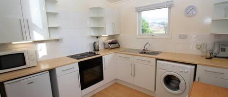 A compact kitchen with white cabinets, a microwave, stove, sink, and a washing machine.