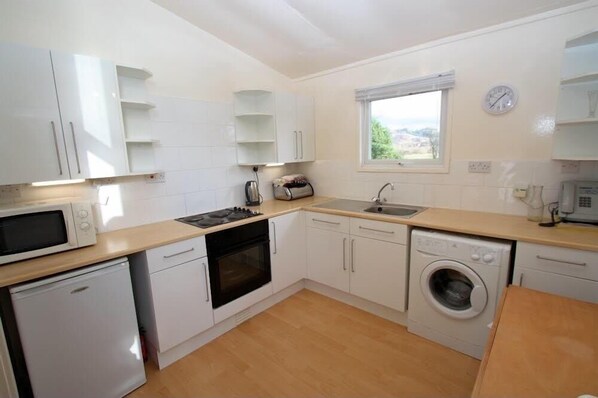 A compact kitchen with white cabinets, a microwave, stove, sink, and a washing machine.