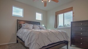 A bedroom with a bed, a dresser, two windows, and a ceiling fan. - Bright and Spacious Home in Quiet Neighborhood - ASTRP260664 (Colorado Springs)