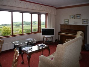 Ein Wohnzimmer mit großem Fenster, Fernseher, Klavier und bequemen Sesseln.