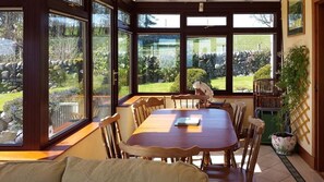 A conservatory with a wooden table and chairs, large windows, and a view of a garden.