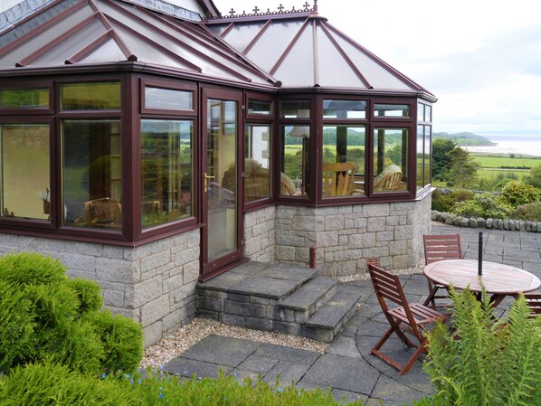 A conservatory with a stone base, large windows, and a view of the countryside.
