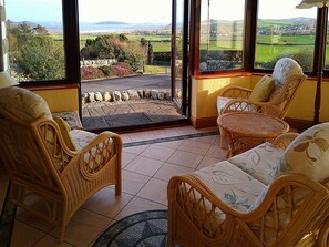 Una habitación con muebles de mimbre, vistas a un paisaje verde y una pared de piedra.