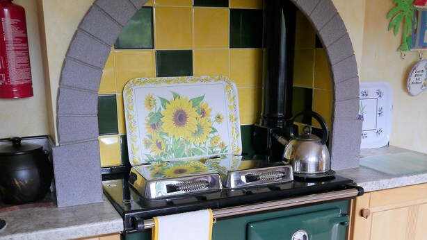 Une cuisine avec un poêle vert, un pare-feu en carreaux et un extincteur.