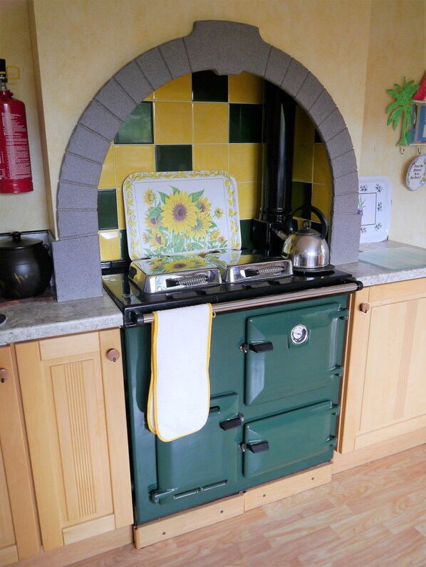 A kitchen with a green stove, a tiled backsplash, and a fire extinguisher.