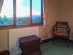 A room with a view through a window, a radiator, a wooden cabinet, a chair, and a trash bin.