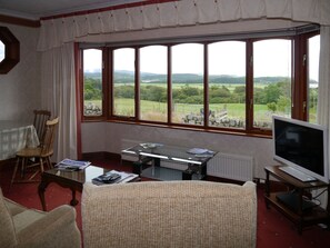 A room with a large window, a television, a table, and a chair.