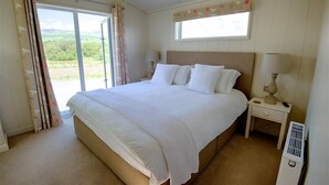 Une chambre avec un grand lit, une table de chevet avec une lampe, une fenêtre donnant sur un paysage verdoyant et un radiateur.
