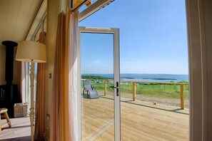 A room with a large sliding glass door leading to a deck with a view of the sea. - Barley Lodge -  a lodge that sleeps 6 guests  in 3 bedrooms (Gatehouse of Fleet)