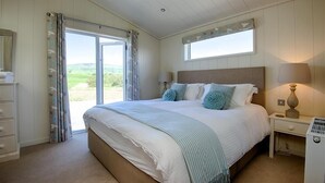 Un dormitorio con una cama grande, una ventana con cortinas, una mesita de noche y una lámpara.