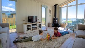 Un salón amplio con un gran ventanal, una chimenea y un televisor sobre un mueble blanco.