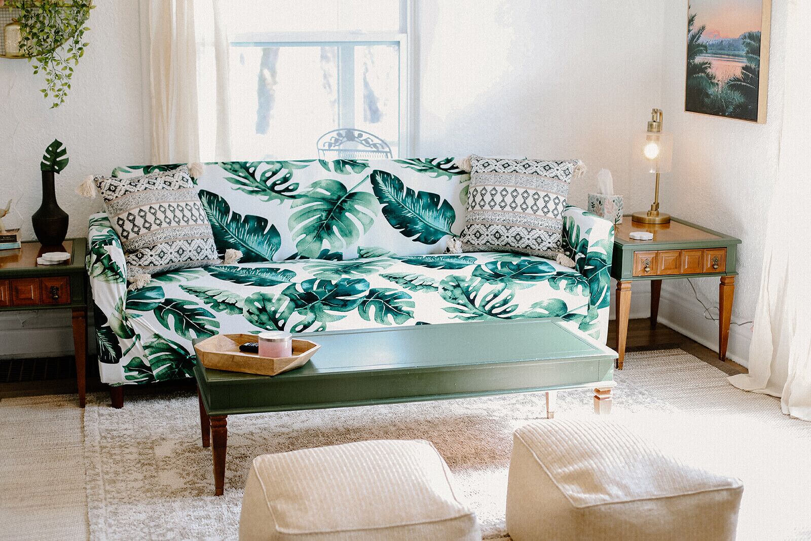 Un salón con un sofá estampado con motivos tropicales, una mesa de centro de madera y una mesita de noche con una lámpara.