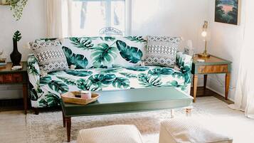Un salón con un sofá estampado con motivos tropicales, una mesa de centro de madera y una mesita de noche con una lámpara.