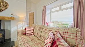 A cozy living room with a plaid sofa, a wooden wall decor, a lamp, and a view of the outdoors through a window. - Threaby Cottage -  a cottage that sleeps 4 guests  in 2 bedrooms (Gatehouse of Fleet)