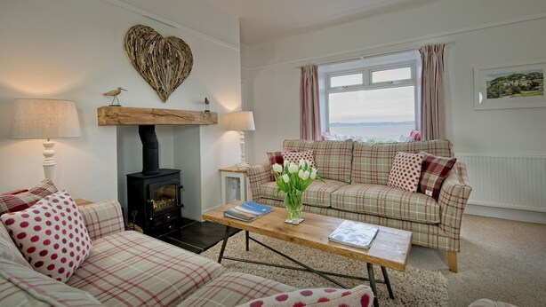 A cozy living room with a fireplace, plaid furniture, and a view of the sea. - Threaby Cottage -  a cottage that sleeps 4 guests  in 2 bedrooms (Gatehouse of Fleet)
