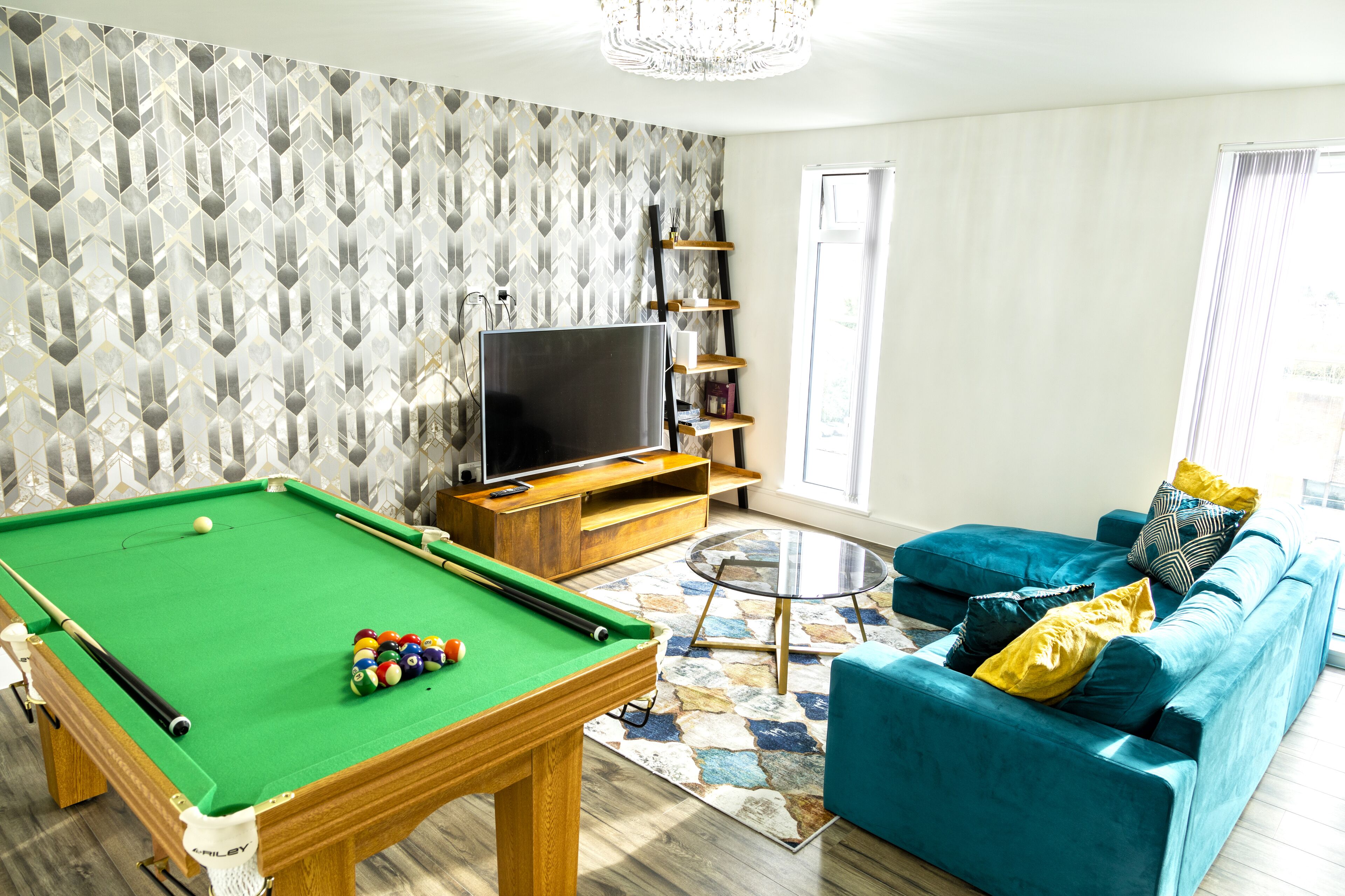 Una sala de estar con mesa de billar, televisor, sofá y un papel tapiz estampado.
