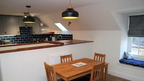 Une cuisine moderne avec une table et des chaises en bois, un îlot central intégré et des luminaires suspendus.