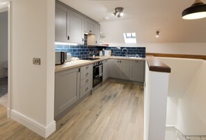 A modern kitchen with grey cabinets, a tiled backsplash, a built-in oven, and a sink. - Stroan - a cottage that sleeps 4 guests in 2 bedrooms (New Galloway)