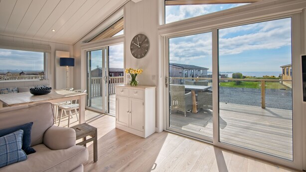 A spacious living area with a large sliding glass door leading to a deck, a dining area with a table and chairs, and a cozy seating area with a sofa.