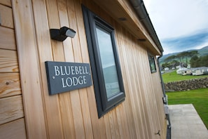 Un mur extérieur en bois avec une enseigne indiquant « BLUEBELL LODGE » et une fenêtre.