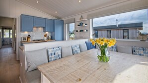 A modern kitchen with blue cabinets, a wooden island, and a dining area with a large table and blue patterned cushions.