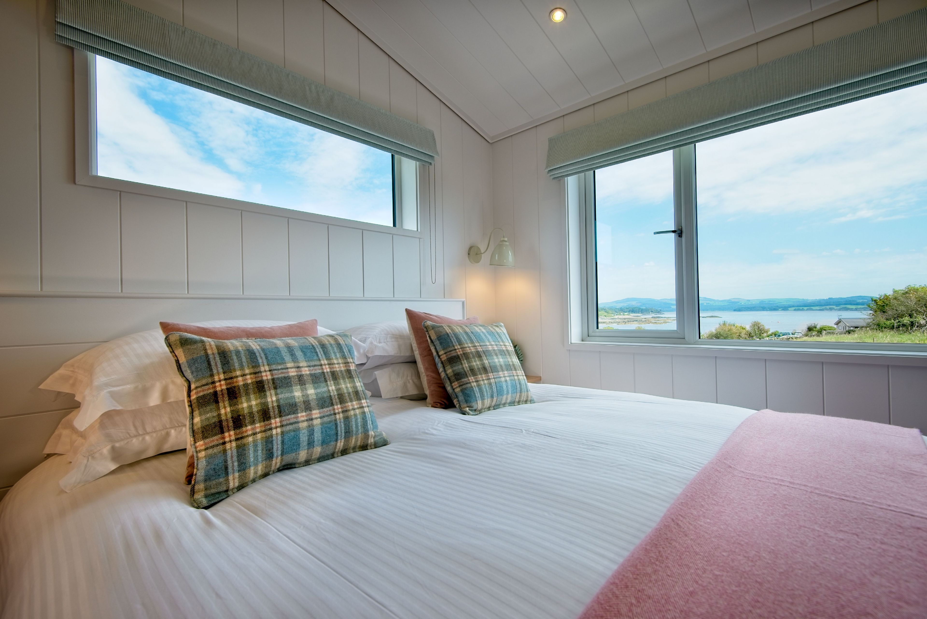 A bedroom with a large bed, two windows, and a view of the landscape.