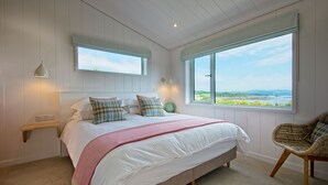 A bedroom with a large bed, two bedside tables, a window with a view, and a chair. - Clover Lodge -  a lodge that sleeps 6 guests  in 3 bedrooms (Gatehouse Of Fleet)