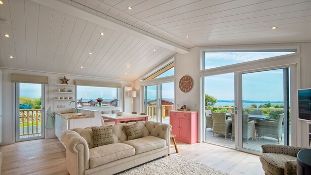 A spacious living area with a large window, a sofa, and a kitchen area. - Clover Lodge -  a lodge that sleeps 6 guests  in 3 bedrooms (Gatehouse Of Fleet)