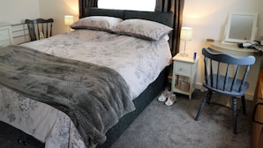 Un lit bien fait, avec une literie à motifs floraux, une table de chevet avec une lampe, une chaise et un bureau avec un ordinateur.