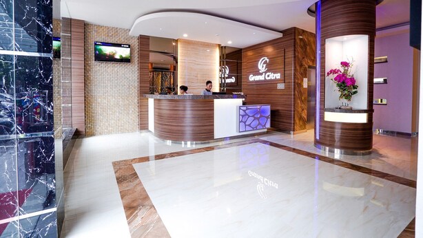 A hotel reception area with a marble floor, a reception desk, a TV screen, and a floral display. - Grand Citra Hotel Makassar By Life (Makassar)
