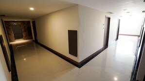 A clean, modern hallway with a marble floor, a wooden accent wall, and a door at the end. - Grand Citra Hotel Makassar By Life (Makassar)