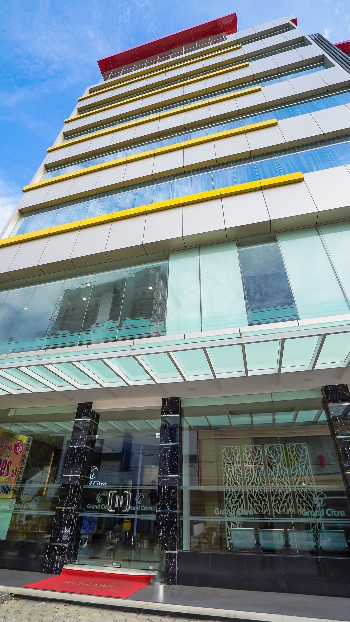 Un edificio moderno con varios pisos, amplios ventanales de vidrio y una entrada destacada con alfombra roja.