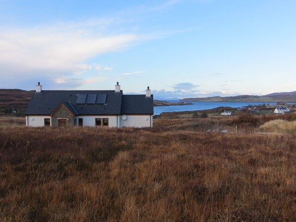 A house with a sloped roof, solar panels, and a view of a lake and hills in the background.