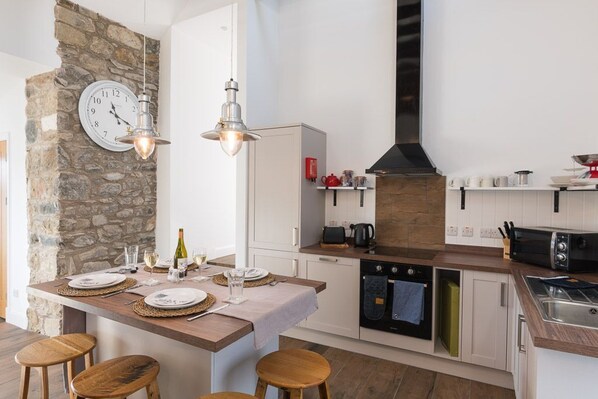 A modern kitchen with a stone accent wall, a built-in stove, and a dining area with stools.