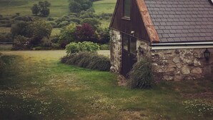 A stone house with a dark roof, surrounded by a lush green landscape and rolling hills. - Dairy Cottage -  a cottage that sleeps 4 guests  in 2 bedrooms (Gatehouse of Fleet)